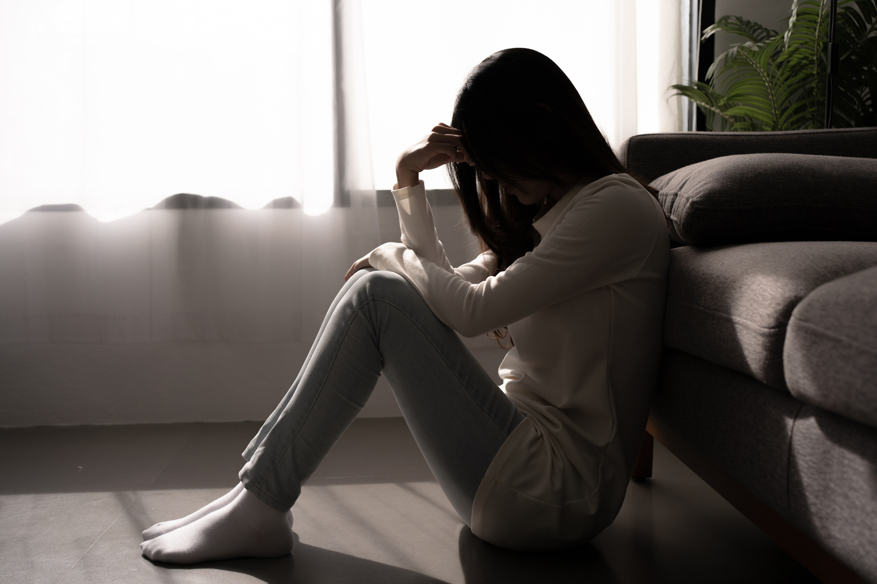 Young woman feeling depressed and stressed sitting in dark bedro